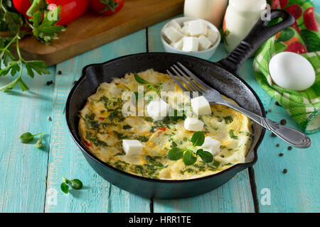 Omelett mit Paprika, Tomaten und Feta-Käse in einer gusseisernen Pfanne auf einem Holztisch. Das Konzept der gesunden Ernährung und Diät. Bulgarische cuis Stockfoto