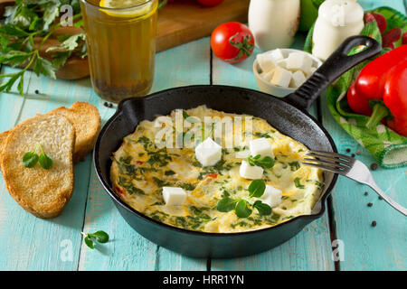 Omelett mit Paprika, Tomaten und Feta-Käse in einer gusseisernen Pfanne auf einem Holztisch. Das Konzept der gesunden Ernährung und Diät. Bulgarische cuis Stockfoto