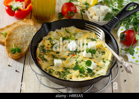 Omelett mit Paprika, Tomaten und Feta-Käse in einer gusseisernen Pfanne auf einem Holztisch. Das Konzept der gesunden Ernährung und Diät. Bulgarische cuis Stockfoto