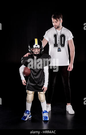 Voller Länge Blick auf junge Spieler des amerikanischen Fußballs stehen mit Ball in der Nähe von Trainer Stockfoto