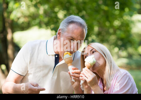 Porträt einer glücklich älteres paar Essen eine schmelzende Eis in einem park Stockfoto