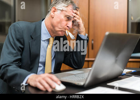 Nervösen Geschäftsmann Rauchen eine Menge von Zigaretten auf einmal beim Blick auf seinen computer Stockfoto