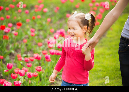 Closeup Portrait glückliche Familie. Kleine lustige Mädchen 4 Jahre alt Spaziergänge Blumenbeet Tulpen an Hand der Mama im Frühjahr Stadtpark. Horizont Stockfoto