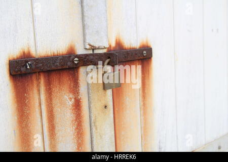 Alte Schleuse und rostiges Eisen Hasp auf eine weiße Holztür mit Rostflecken liefen die Tür. Stockfoto
