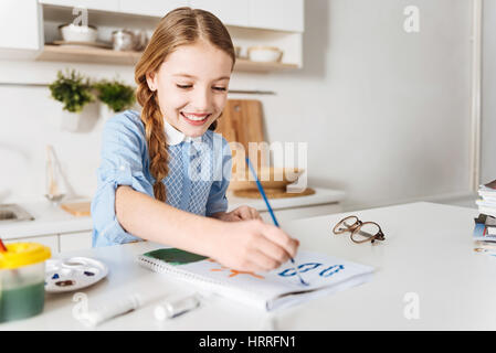 Wooly und blau. Neugieriges freudige kreative Kind üben ihre künstlerischen Fähigkeiten mit Wasserfarben für die Erstellung von blauem Himmel sitzend am Tisch in einem Stockfoto