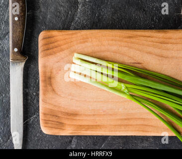 Ein paar Frühlingszwiebeln auf ein Schneidebrett. Hintergrund schwarz Schiefer. Stockfoto