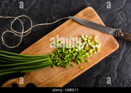 Ein paar Frühlingszwiebeln auf ein Schneidebrett. Hintergrund schwarz Schiefer. Stockfoto