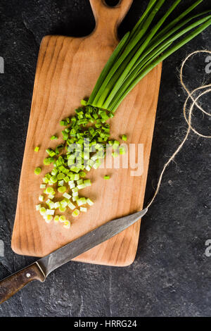 Ein paar Frühlingszwiebeln auf ein Schneidebrett. Hintergrund schwarz Schiefer. Stockfoto