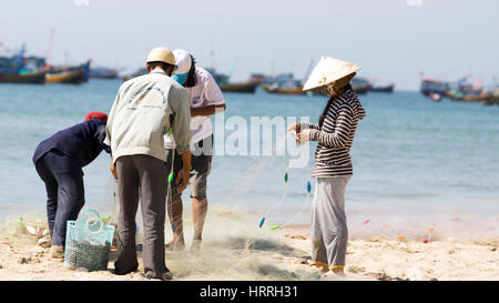 Vier Fischer Fisch aus ihre Netze und setzen sie in Körbe am Strand am Morgen, Vietnam. Stockfoto