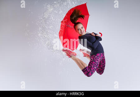 Frau im Sprung mit einem Regenschirm. Gefrorene Bewegung. Stockfoto