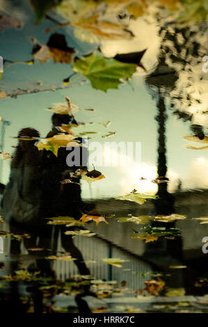 Silhouetten von Menschen zu Fuß spiegelt sich im Wasser während der regnerischen Tag in der Stadt Stockfoto