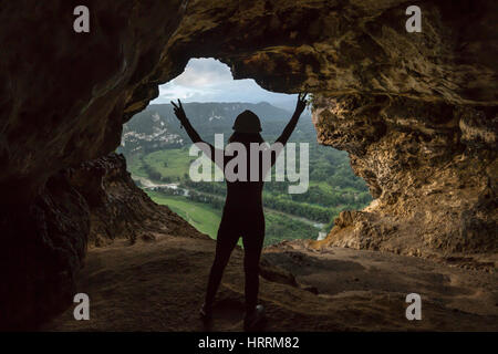 JUNGE FRAU STEHT ANHEBEN ARME SIEG HÖHLE FENSTER MIT BLICK AUF RIO GRANDE VALLEY DE ARECIBO PUERTO RICO Stockfoto