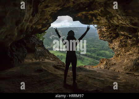 JUNGE FRAU STEHT ANHEBEN ARME SIEG HÖHLE FENSTER MIT BLICK AUF RIO GRANDE VALLEY DE ARECIBO PUERTO RICO Stockfoto