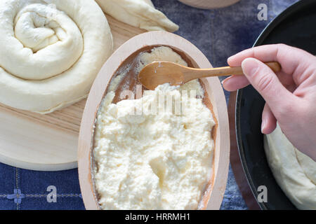 Weibliche Hand hob geschmolzenen Käse aus Holzschale. Käsekuchen auf der Holzplatte sichtbar Stockfoto