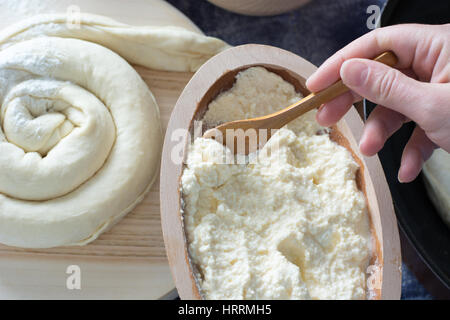 Weibliche Hand hob geschmolzenen Käse aus Holzschale. Käsekuchen auf der Holzplatte sichtbar Stockfoto