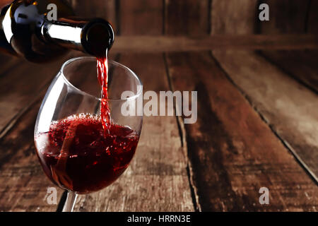 Rotwein im Glas auf hölzernen Hintergrund. Schöne Alkohol Hintergrund. Rotwein aus der Flasche gießen. Freiraum für Text auf hölzernen Hintergrund. Stockfoto