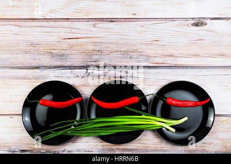 Rote Paprika auf schwarzen Schale. Frühlingszwiebeln auf schwarzen glänzenden Platten. Gemüse in Platten über hölzerne Hintergrund. Bunten Nahrung Hintergrund. Freiraum für t Stockfoto