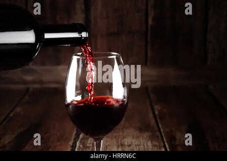 Wein im Glas auf braunem Hintergrund aus Holz. Rot Wein gießen aus Flasche. Nahaufnahme von roten Wein Splash. Hintergrund mit Rotwein ablöschen. Stockfoto