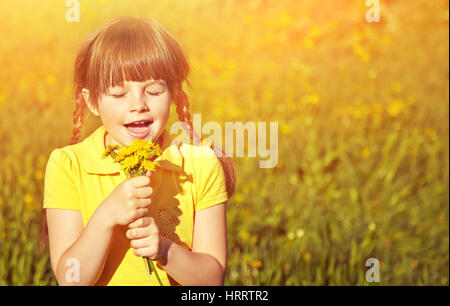 ein sehr glücklich kleines Mädchen mit einem Blumenstrauß in Händen auf Hintergrund von grünem Rasen. Kind im Freien mit Löwenzahn Stockfoto