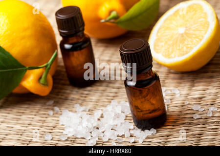 Flasche mit Zitrone ätherisches Öl, frischen Zitronen auf Stroh Hintergrund Stockfoto