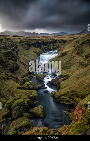 Oberen Fluss Skoga Wasserfall mit Sturmwolken über Berge im Hintergrund, Island Stockfoto