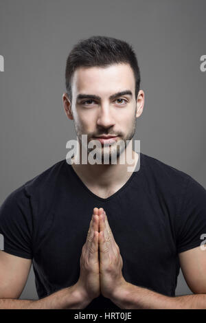 Junge Fitness Männermodel berühren hand Palmen Namaste-Geste. über dunkle graue Studio-Hintergrund. Stockfoto