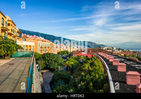 Los Cancajos, La Palma. Ein Blick vom Hotel Las Olas Ferienwohnungen suchen entlang der Küste in Richtung Santa Cruz ein paar Kilometer entlang der Küste. Die gelbe Hotel Fronten führen zum weit entfernten Küste, während die Dächer von niedrigeren Gebäuden Kurve in unten rechts auf das Foto. Es ist eine klare sonnigen Morgen mit nur ein paar leichte trübe Wolken über dem Meer zum Verweilen ein. Mit einer Ricoh GRII Kamera fotografiert. Stockfoto