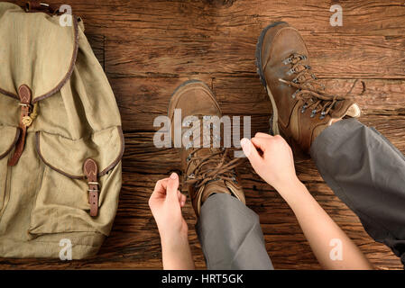 Junge Frau setzt sich auf Schuhe zum Wandern auf Holzboden Stockfoto