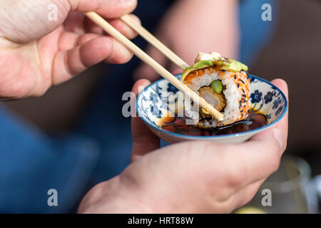 Männliche Hand, die Stäbchen Sushi-Rolle in die Sojasauce Tauchen Stockfoto