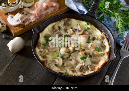 Omelette aus Wachteleier mit Schinken und Speck in einer Pfanne aus Gusseisen auf einem Holztisch. Das Konzept der gesunden Ernährung und Diät. Stockfoto
