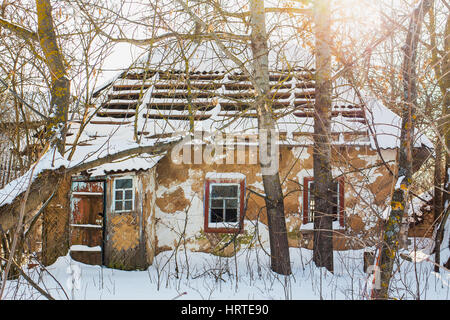 Alte verlassene leer aus Holz braun Landhaus mit gebrochenen Dach und Fenster mit frischen weißen Schnee bedeckt. Dorf in der Ukraine. Horizontale Farbbild. Stockfoto
