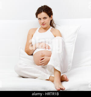Junge schwangere Frau auf dem Sofa sitzen Stockfoto