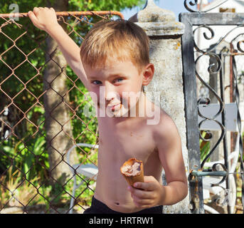 Der schmutzige kleine Junge isst Eis im Sonnenuntergang leuchten Stockfoto