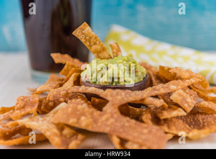 Haufen von Chips Surround Guacamole mit Cola im Hintergrund Stockfoto