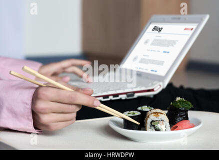 Asiatische Sushi Set und Frau arbeitet auf Laptop-Computer, die Einnahme von Nahrung Rollen mit hölzernen Stäbchen Stockfoto