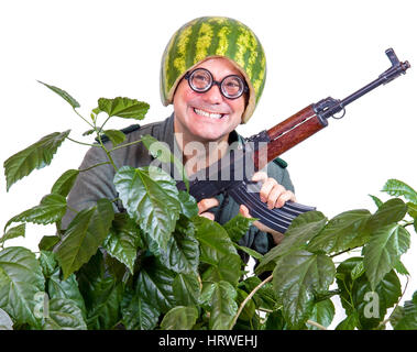 Lustige heitere Soldat mit einem Maschinengewehr aus den Blättern kleben. Verrückter Mann in einem Helm der Wassermelone patrouillieren mit Waffe in seinen Händen. Stockfoto