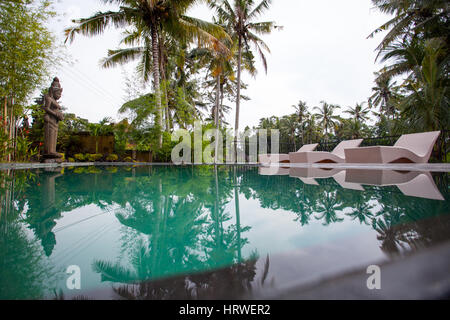 Pool auf einem Hintergrund von Palmen und Sonnenliegen mit einer Steinstatue in einem tropischen Land Stockfoto