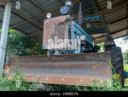 Schmutzige alte Traktor unter einem Schuppen auf dem Hof geparkt Stockfoto