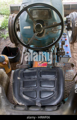 Blick ins Innere eines gebrauchten Traktors mit einem Lenkrad und die Steuerplatine. Schmutzige alte Traktor unter einem Schuppen auf dem Hof geparkt Stockfoto