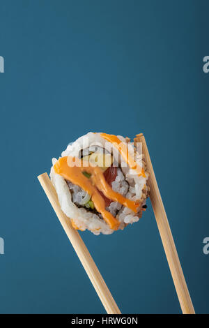 Einzigen Stück Sushi in hölzernen Stäbchen vor einem blauen Hintergrund statt Stockfoto