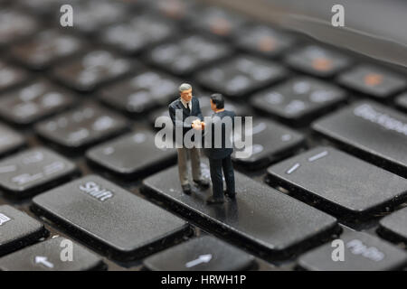 Selektiven Fokus Miniatur Business Mann Handshake auf der Taste Enter Taste Tastatur Laptop als Engagement und Partnerschaft Konzept. Stockfoto