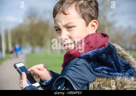 Ein kleiner Junge spielt Pokemon gehen auf einem Handy draußen im Park. Stockfoto