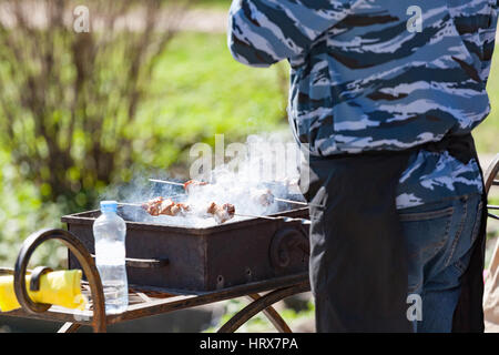 der schöne Rauchen Schaschlik auf einem Kohlenbecken am Ufer eines Reservoirs Stockfoto