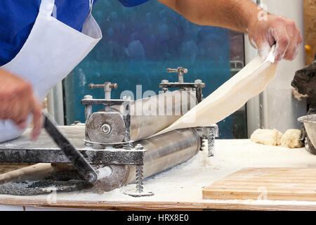 Männer Händen ausrollen Teig hautnah. Mann, Teig vorbereiten, Kochen von Teigwaren auf einem Holztisch im café Stockfoto