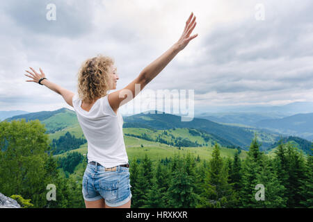 Junge Frau am Rande der Klippen stehen und blickte auf einen Himmel mit erhobenen Händen Stockfoto