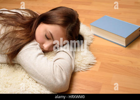 Junge Frau schläft auf dem Boden vor einem Buch Stockfoto