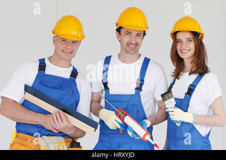 Fröhliche Mitarbeiter in Uniform und Schutzhelme mit Werkzeugen Stockfoto