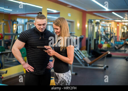 Passen Sie attraktives junges Paar in einem Fitnessstudio, einem Tablet-pc zu betrachten, wie sie ihre Fortschritte und Fitness überwachen Stockfoto