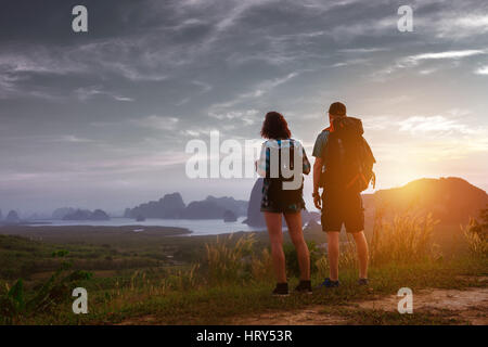Paar von Rucksacktouristen steht bei Sonnenaufgang oder Sonnenuntergang am Meer und Inseln Kulisse. Tourismus-Konzept Stockfoto