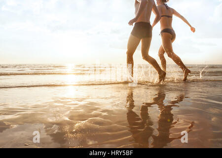 glückliches junges Paar läuft bis zum Meer am Strand bei Sonnenuntergang, Silhouetten von Mann und Frau, Urlaub mit der Familie Stockfoto